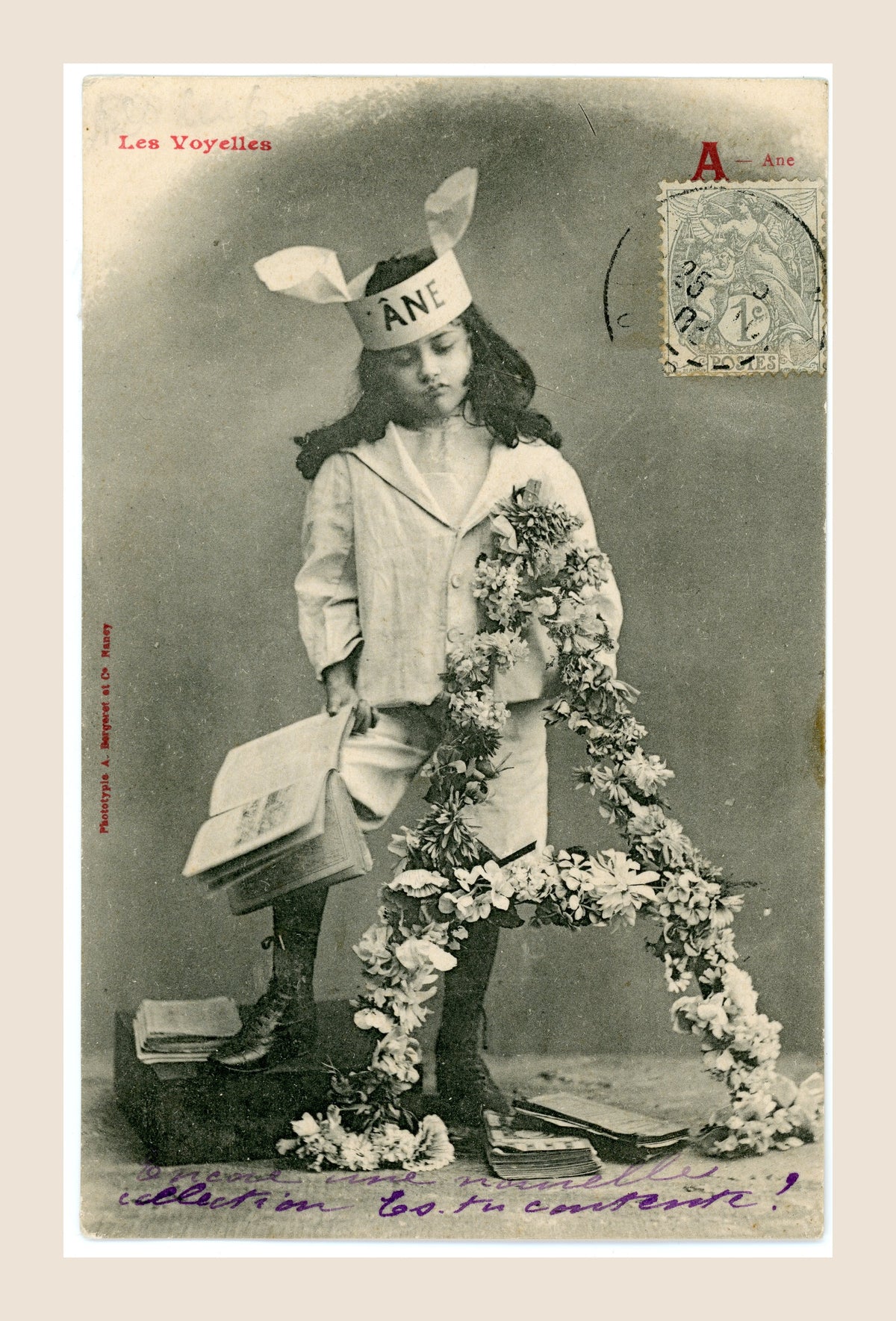 Antique French Bergeret postcard Les Voyelles, letter A for Âne, showing a young girl in a donkey-ear bonnet with books and floral decoration, circa 1905.
