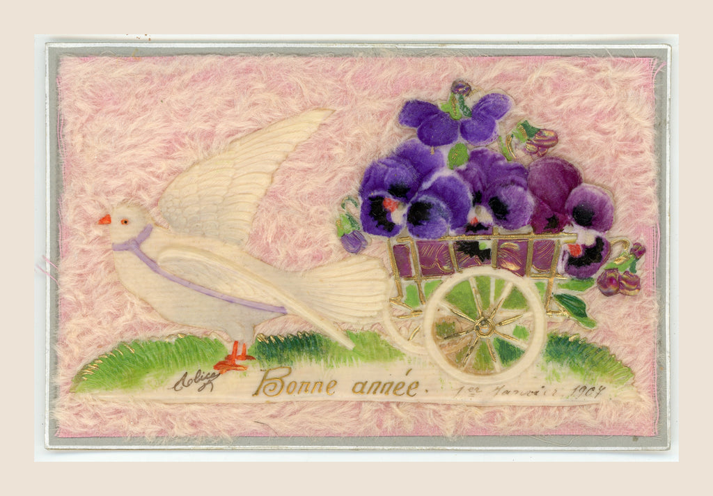 Antique New Year postcard with a white dove pulling a cart of purple fabric pansies in relief on a soft pink textile background, with “Bonne année” below.