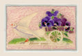 Antique New Year postcard with a white dove pulling a cart of purple fabric pansies in relief on a soft pink textile background, with “Bonne année” below.