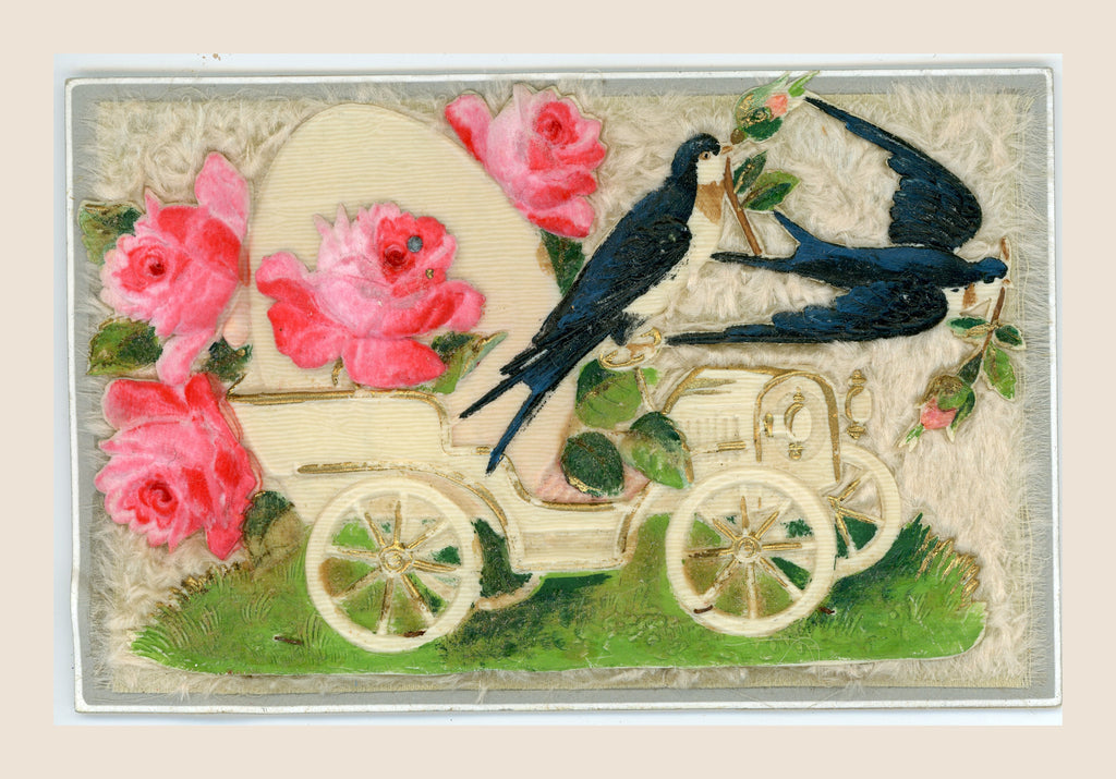Antique postcard with a cream-coloured early motor car, two blue swallows and pink roses in relief on a pale fibrous textile background.