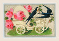 Antique postcard with a cream-coloured early motor car, two blue swallows and pink roses in relief on a pale fibrous textile background.