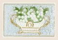 Antique postcard with white lily of the valley flowers in an ornate white and gold jardinière, in relief on a pale blue fibrous textile background.