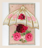 Antique postcard with a movable cream parasol spread beyond the card edges, gold and silver details, and fabric roses on a soft pink textile background.