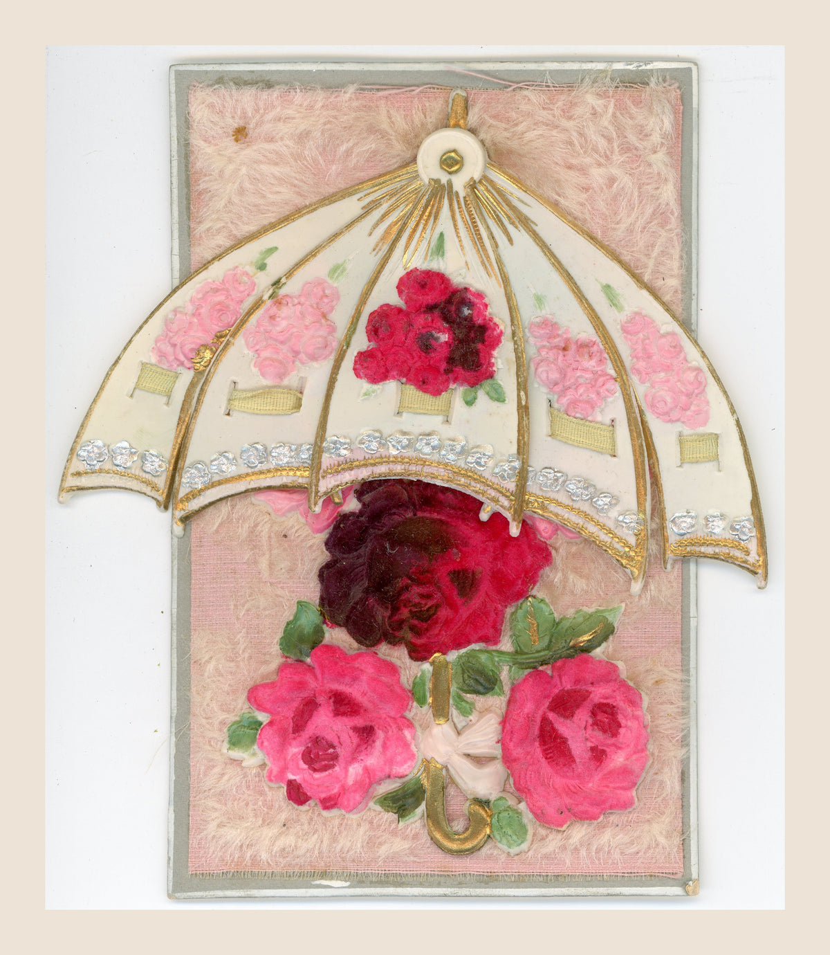 Antique postcard with a movable cream parasol spread beyond the card edges, gold and silver details, and fabric roses on a soft pink textile background.