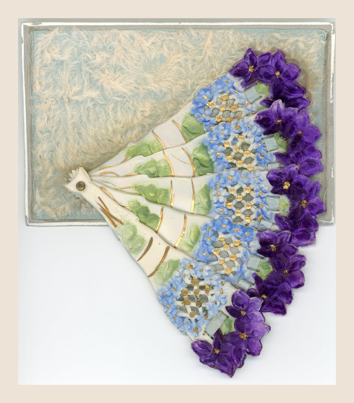 Antique postcard with an open folding fan, purple and pale blue flowers, gold-coloured details and a soft textile background.