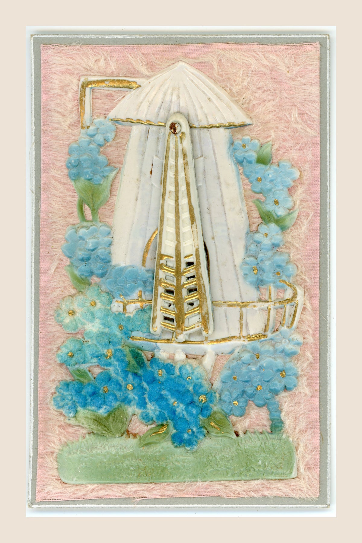 Antique windmill postcard with its movable sails gathered vertically over the tower, blue floral decoration and gold-toned details on pink textile.