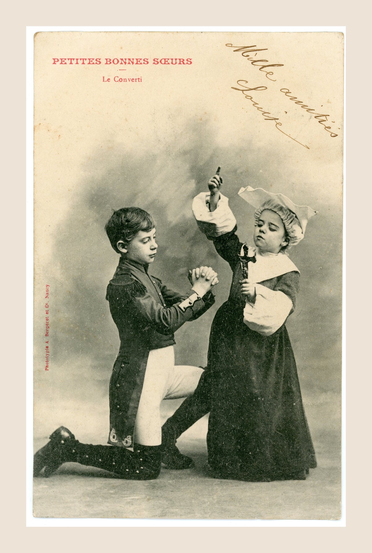 Antique Bergeret Petites Bonnes Sœurs Le Converti photographic postcard depicting a kneeling boy praying before a girl dressed as a nun holding a crucifix.