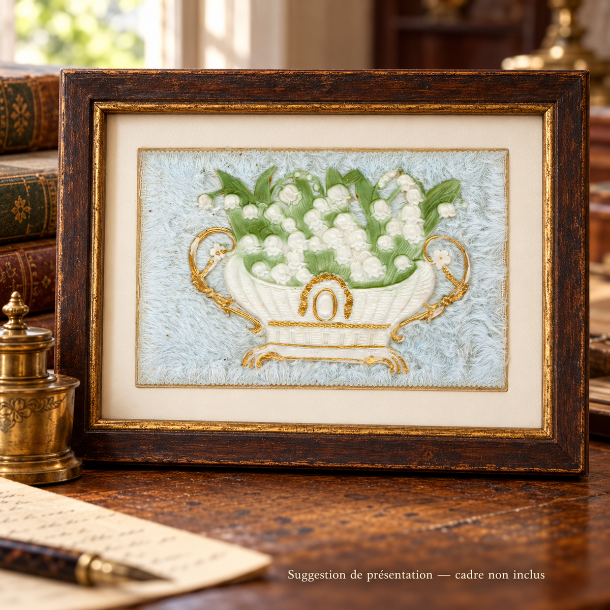 Antique lily of the valley postcard with a white and gold jardinière on pale blue textile, displayed in a patinated wooden frame on a vintage writing desk. Frame not included.