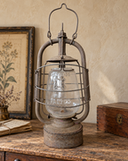 Styled scene of an unlit Panzer Cuirass lantern on an aged wooden console beside old letters, a botanical print and a wooden box.