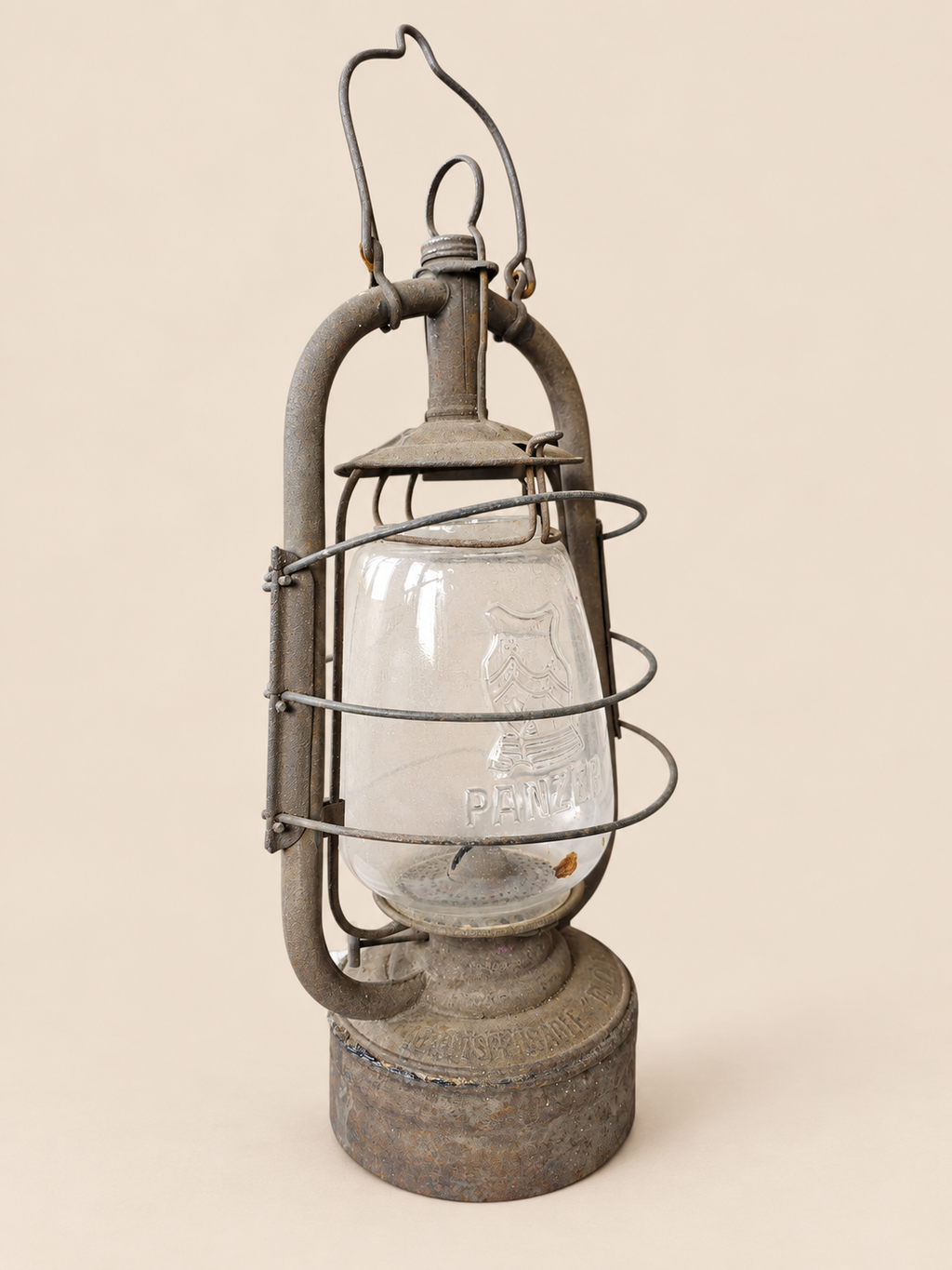 Three-quarter front view of a vintage Panzer lantern with embossed glass, raised carrying handle and weathered metal base.