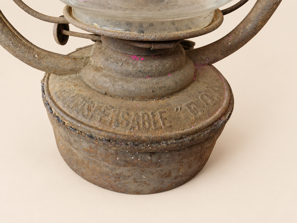 Close-up of the Panzer lantern’s metal reservoir, showing embossed lettering, worn finish, small pink marks and the irregular seam.