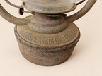 Close-up of the Panzer lantern’s metal reservoir, showing embossed lettering, worn finish, small pink marks and the irregular seam.
