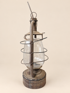 Side profile of a vintage Panzer hurricane lantern with raised handle, curved metal support, wire cage and glass globe.