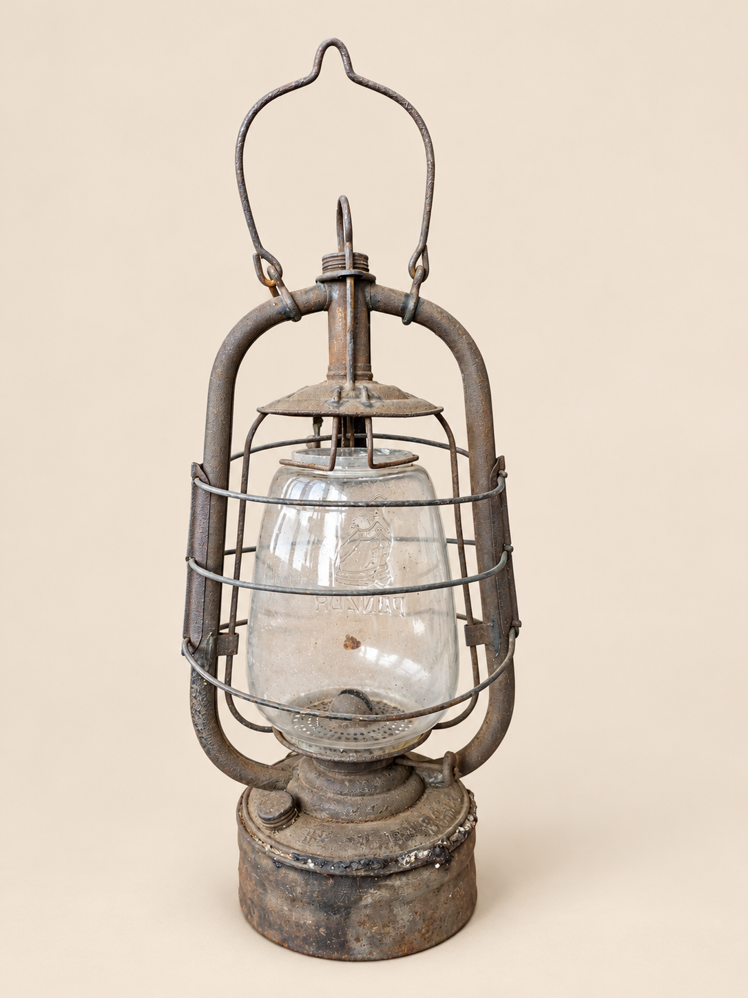 Rear view of a vintage Panzer hurricane lantern with raised handle, glass globe and weathered metal reservoir on a cream background.